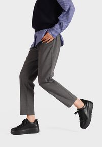 Pantaloni grigi su misura abbinati a una camicia a quadri blu e scarpe da ginnastica con plateau nere. L'outfit presenta linee pulite e una silhouette moderna.