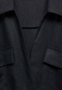 Gros plan sur un tissu gris foncé montrant un col à revers et deux poches à rabat sur une veste ou un manteau tailleur.