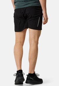 Svarta idrottsshorts med en slät yta, med en reflexrand, i kombination med svarta sportskor med en texturerad sula.