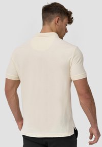 Cremfarbens Poloshirt aus strukturiertem Stoff. Verfügt über einen klassischen Kragen, kurze Ärmel und einen seitlichen Schlitz am Saum für mehr Bewegungsfreiheit.