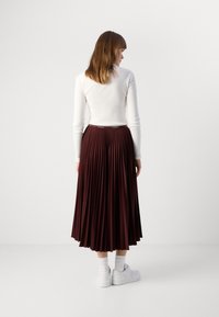 Jupe plissée bourgogne avec une taille large, associée à un haut blanc à manches longues, portée avec des baskets blanches et des chaussettes de longueur cheville.