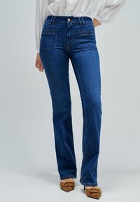 Vaqueros de mezclilla azul oscuro con cintura entallada, piernas rectas y dos bolsillos traseros. Presentan herrajes dorados y detalles de costura sutiles.