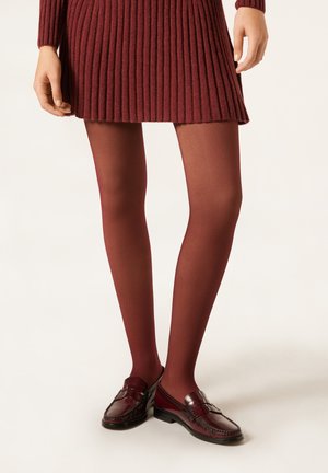 Collants bordeaux associés à une robe côtelée et des mocassins foncés. Les collants sont semi-opaques, avec une texture lisse et une coupe ajustée.