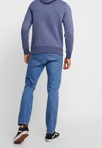 Marinblå hoodies, blå denimjeans, svartvita sneakers. Jeansen har en rak passform med distinkta bakfickor och sömnadsdetaljer.