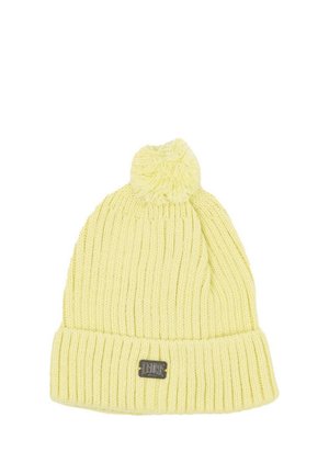 Gorro de punto acanalado de color amarillo pálido, con el borde doblado, un pompón mullido y una pequeña etiqueta oscura, sobre un fondo blanco.