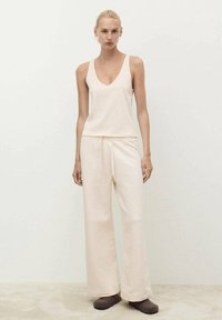 Helles beiges Tanktop mit V-Ausschnitt, kombiniert mit lockeren, passenden Schlaghosen. Weicher Stoff, dezente Textur und ohne Muster.
