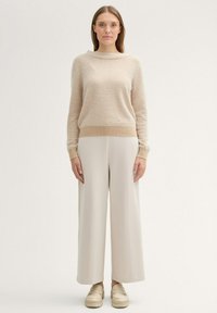 Beiger gestreifter Pullover mit rundem Halsausschnitt, kombiniert mit hellbeigen weiten Hosen und klobigen cremefarbenen Slippern. Einfaches und sauberes Design.