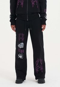 Zwarte sweatpants met paarse tribale patronen en graphics, waaronder een ontwerp van een schedel en hart, gemaakt van zacht materiaal, met een trekkoord in de taille.
