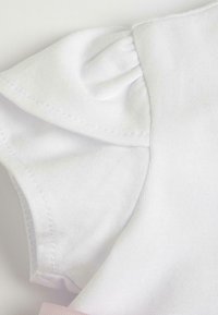 Tessuto di cotone bianco con dettagli di maniche arricciate. Texture liscia, con cuciture ordinate e un accento rosa chiaro all'orlo.