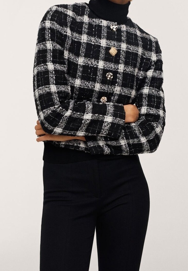Pull boutonné à carreaux noir et blanc avec tissu texturé, porté sur un col roulé noir, associé à un pantalon noir ajusté.