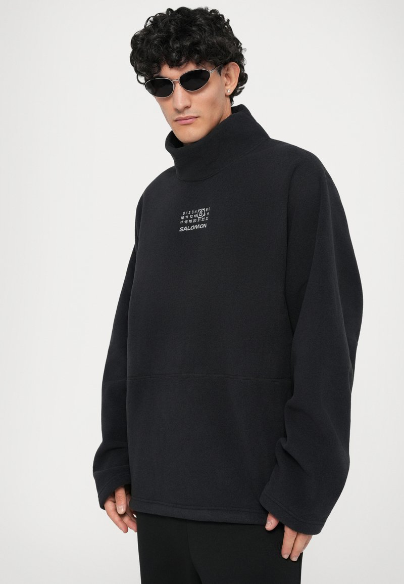 Black fleece pullover with a high collar and embroidered logo. Features long sleeves and a relaxed fit. Smooth, soft texture.