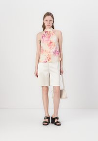 Blomster halterneck topp i pastellfarger, hvite shorts og svarte sandaler med spenner. Har intrikate blomsterdesign og avslappet passform.