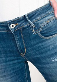 Jeans in denim blu scuro con una finitura sbiadita. Le caratteristiche includono tasche cucite, chiusura con bottone e un anello per la cintura.