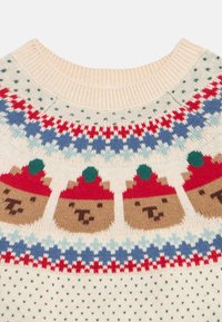 Πουλόβερ σε κρεμ απόχρωση με πλεκτό σχέδιο από πρόσωπα αρκούδων που φορούν κόκκινα καπέλα, διακοσμημένο με γεωμετρικά σχέδια σε μπλε και κόκκινο.