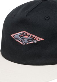 Svart baseballcap med en krämfärgad skärm, med en broderad grå och orange grafik i en diamantform på framsidan.