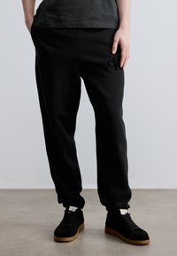 Μαύρη φόρμα από μαλακό ύφασμα, με ρυθμιζόμενο ζωνάρι στη μέση και μικρό κεντημένο λογότυπο CK στο πλάι.