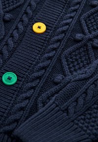Pletený cardigan v námořnické modři s texturovanými vzory, designem kabelového pletení a třemi barevnými knoflíky: žlutým, zeleným a modrým.