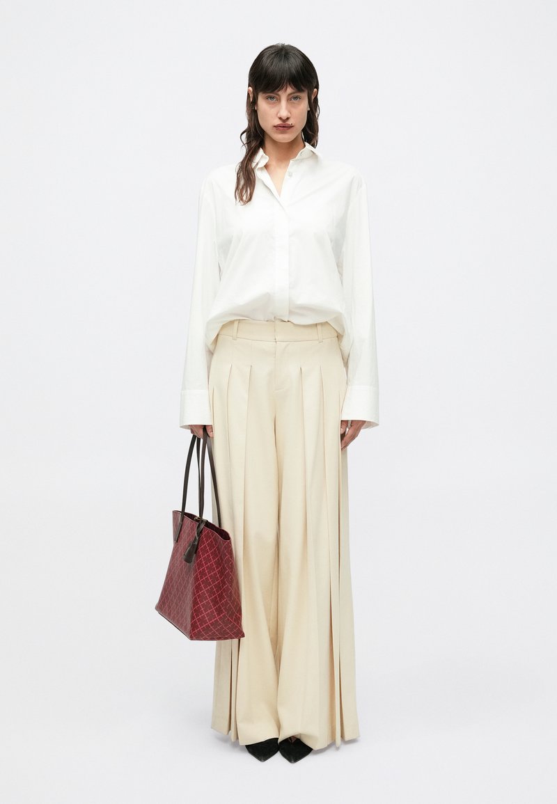 Weißes Hemd mit Knopfleiste, cremefarbene plissierte Hose und eine rote geometrische Tragetasche. Dicke schwarze Absätze vervollständigen das Outfit. Minimalistisches Design.