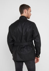 Black, belted jacket with a high collar, featuring a smooth texture and button accents on the cuffs. Rear view shows a relaxed fit.