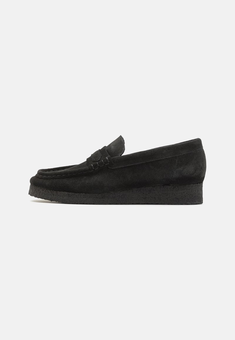 Black suede loafers feature a textured upper, back seam detail, and a low, sturdy rubber sole for comfort and durability.