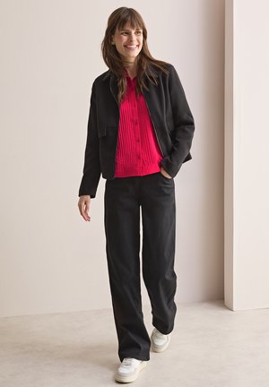 Chaqueta negra con cremallera, blusa roja texturizada con botones, pantalones anchos negros y zapatillas blancas. Materiales suaves y diseño casual.