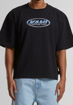 T-shirt en coton noir à manches courtes avec un logo ovale réfléchissant bleu "KANI" sur le devant. Coupe décontractée avec un ourlet droit.