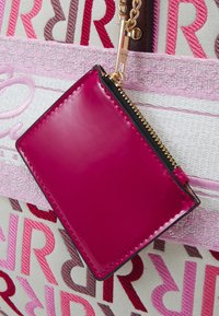 Fuchsia patentläder-korthållare med dragkedja, fäst vid en tygpåse med broderade flerfärgade bokstäver i varierande storlekar.