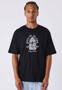Camiseta de algodón negra con un diseño gráfico en el frente que presenta elementos coloridos y el texto "Alcanza las Estrellas" y "Proyecto X Piezas".
