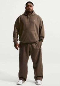 Sweat à capuche en coton marron avec une poche avant et un cordon de serrage, associé à un pantalon de survêtement assorti. Présente un petit logo Nike blanc sur la poitrine.