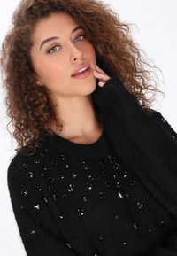 Fekete kötött pulóver, texturált felülettel, kerek, fényes flitterekkel, különböző mintákban elrendezve az elején.