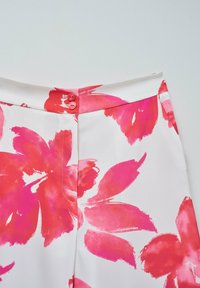 Pantalons à imprimé floral avec une base blanche, présentant de grandes fleurs roses et rouges. Agrémentés de deux boutons roses à la taille.