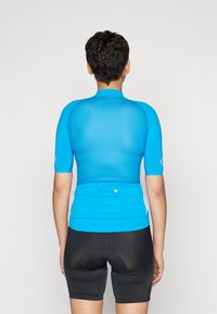 Maillot de cyclisme bleu à manches courtes, avec une texture lisse, un design ajusté, des coutures plates et une poche arrière. Associé à un short noir rembourré.