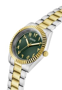 Montre en acier inoxydable doré et argenté avec un cadran vert ; boîtier arrondi, lunette crantée, chiffres arabes dorés et bracelet à maillons.