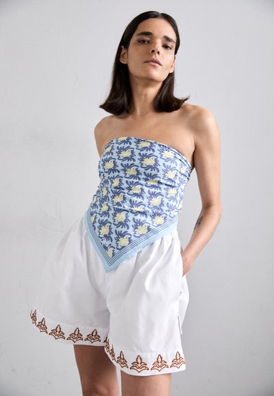 Strapless top featuring a light blue floral pattern with yellow accents and a triangular shape. Paired with white shorts adorned with brown embroidery.