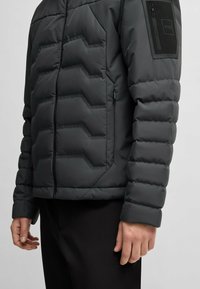 Fleecefodrad jacka i mörkgrått, med kviltad textur, framtill dragkedjestängning och en dragkedjeficka på vänster ärm. Slim fit-design.