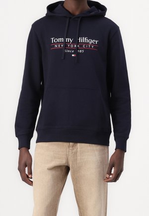Navyblå hoodie med en frontlomme, justerbar snøre og et logo med "Tommy Hilfiger, New York City" i hvid og rød tekst.