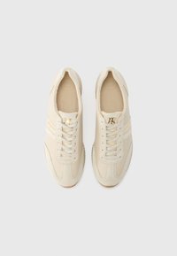 Baskets beige avec une tige en cuir lisse, fermeture à lacets et accent logo doré ; bout arrondi, semelle en caoutchouc texturée et coutures minimalistes.