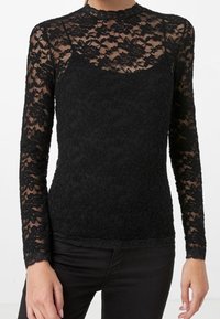 Svart långärmad topp i spets med hög halsringning, blommönster och en figurnära silhuett. Fodrad med ett solidt svart lager under.