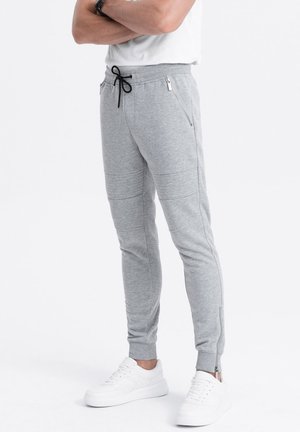 Gray sweatpants with a tapered fit, featuring zippered pockets and ankle zippers, made from a soft, textured fabric. Paired with white sneakers.
