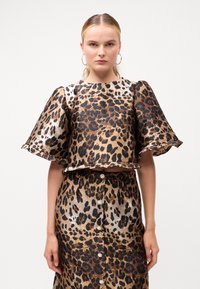Top og skjørt sett med leopardmønster, med en cropped design, flagrende ermer og knappdetaljer i nyanser av brunt og svart. Glatt tekstur.