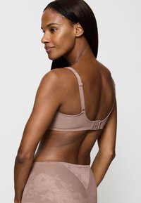 Beha van zacht beige stof met bloemrijke textuur, verstelbare bandjes en een haaksluiting aan de achterkant. Eenvoudig, gestroomlijnd ontwerp.