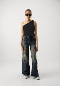 Bodysuit noir à une épaule associé à un pantalon cargo en denim bleu à jambes larges, doté de poches et d'un lavage vintage, complété par des baskets noires.