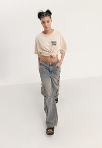 Cream cropped t-shirt with "SELF CARE" text, paired with light blue cargo jeans featuring pockets. Model wears black platform sandals.
