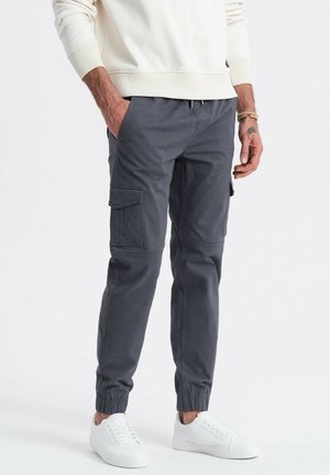 Pantaloni cargo in tessuto grigio con orli a maniche, tasche laterali e vestibilità rilassata, abbinati a sneaker bianche e a una felpa di colore chiaro.