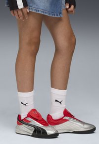 Baskets de sport Puma avec une combinaison de couleurs argent, rouge et noir ; tige texturée avec des rayures distinctes. Portées avec des chaussettes blanches arborant le logo.