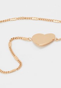 Gold-colored heart pendant necklace with a twisted chain, featuring a smooth, shiny surface and delicate clasp details.