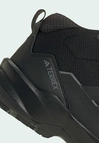 Czarne sneakersy Adidas Terrex z teksturowaną i siateczkową cholewką, grubą podeszwą, pętelką na pięcie oraz widocznym logo z boku.