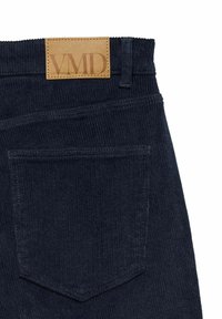 Mornarski kord pantaloni s kožnom oznakom s natpisom "VMD." Uključuje stražnji džep s prošivenim detaljem i teksturiranom površinom.