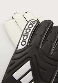 Black and white adidas goalkeeper gloves feature padded fingers, textured surface, and a prominent logo along the wrist strap.
