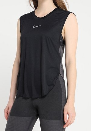 Femme portant un haut de sport noir sans manches Nike et des leggings gris foncé texturés, debout avec une main détendue le long du corps.